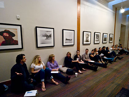Sierra Nevada University fine arts students and faculty sit along the walls of a gallery discussing the student work displayed.