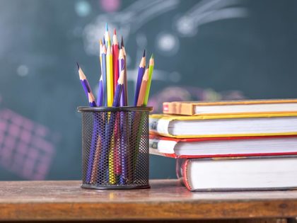 Colored pencils on a table in front of a chalkboard next to some books in a stack. Teacher education at Sierra Nevada University