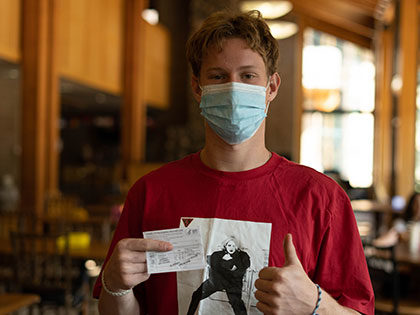 COVID-19 - a masked SNU student holds up his vaccination card