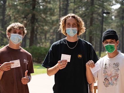 3 masked Sierra Nevada University students hold up their COVID-19 immunization cards