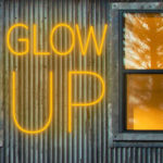 Glow Up fine arts alumni exhibition logo image of glowing amber neon on the Holman Arts and Media Center