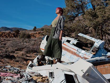 artist Dejaneri Maestas, photo of the artist atop wreckage in the high desert for BFA exhibition 'Liberation NOT Loss'