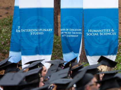 graduates in their mortar boards can be seen below academic banners at the 2019 Sierra Nevada College Commencement