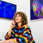 Artist, writer, and educator Julie Weitz, wearing a sweater as colorful as her art, in front of her color photographs.