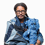 Cuban-American textile artist Llane Alexis wearing - and holding - two of his pieces built from discarded denim scraps.