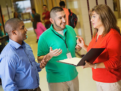 teachers and their principal talk in the school hallway